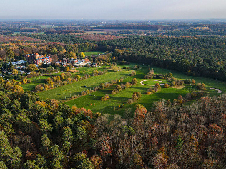 Ein Vogelperspektive auf einen Golfplatz umgeben von Bäumen und sattem Grün.