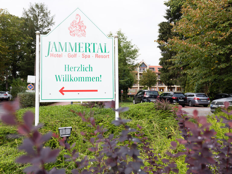 Ein Schild vor einem Gebäude entfaltet eine herzliche Einladung zum JAMMERTAL Hotel Golf Spa Resort.